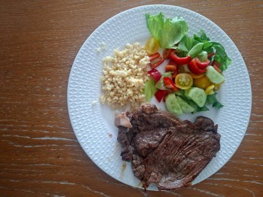 Sebzeli biftek ve ahşap bir masada baharat.