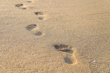 Gün boyunca plaj, dalga ve ayak izleri. Sahildeki suyun yakınındaki kumda insan ayağının ayak izleri..