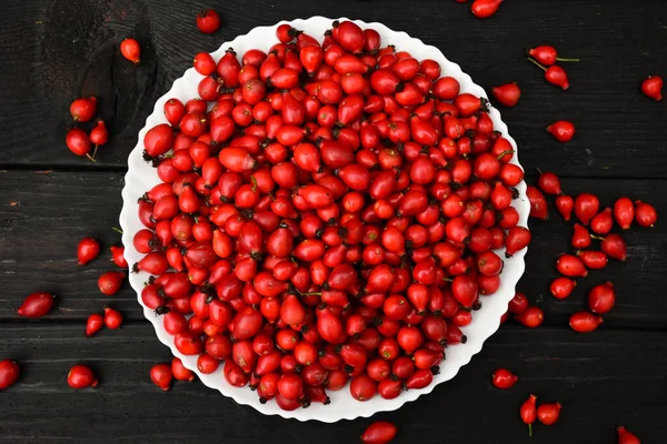 Koyu ahşap arka planda bir tabakta gül ağacı meyveleri. Rosa canina taze kırmızı meyveler. Yüksek kalite fotoğraf