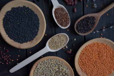 Lentils beans and rice. Organic gluten free dry cereals and legume on black wood background. Black lentils, green lentils and orange lentils on wooden plates and black, wild rice, red rice and brown