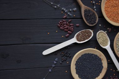 Lentils beans and rice. Organic gluten free dry cereals and legume on black wood background. Black lentils, green lentils and orange lentils on wooden plates and black, wild rice, red rice and brown