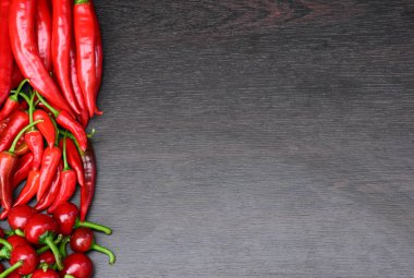 Kırmızı acı biber yığını, yazı için boşluk ile sınırdır. Koyu ahşap arka planda izole edilmiş kırmızı kırmızı kırmızı biber. Kiraz ve küçük acı biber.