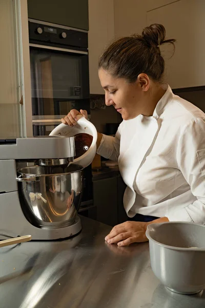 medium-adult woman pastry chef adding chocolate in planetary mixer, owner of her own business