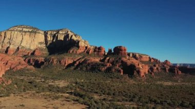 Bear Dağı ve etrafındaki kaya oluşumları öğleden sonra Sedona, Arizona yakınlarında. Havadan çekim ağaçların üzerinden dağlara doğru uçuyor.. 