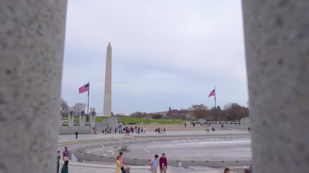 観光客は冬の終わりにワシントンDcのナショナルモールで第二次世界大戦記念碑を訪問します ワシントン記念碑は遠くに見られる 記念碑を明らかにするために列の開口部の間にカメラドル — ストック動画