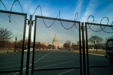 6 Ocak 2021 'deki ayaklanmadan sonraki aylarda güvenlik endişelerini gidermek için dikenli tellerle çevrili metal bir çitin arkasında, gün batımında Amerikan Kongre Binası. Washington, DC.