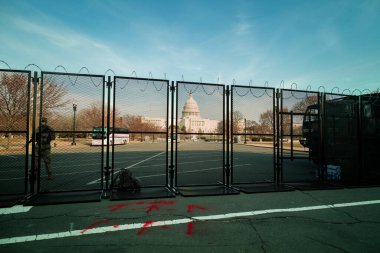 Bir Ulusal Muhafız askeri Washington, DC 'deki Amerikan Kongre Binası' nda nöbet tutuyor. 6 Ocak 2021 'deki ayaklanmanın ardından dikenli tellerle çevrili metal bir çitin arkasında gün batımında.. 