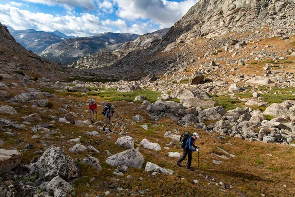 Üç erkek gezgin Wyoming 'deki Wind River Sıradağları' ndaki Douglas Tepesi 'nin güneyinde yürüyüş yapıyor. Uzakta, Yukarı Altın Göl (10176 Gölü) ve Louise Gölü (10161 Gölü) havzası görülür..