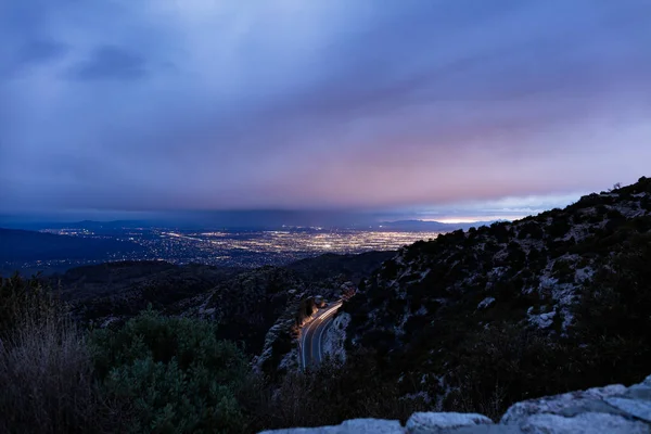Tucson, Arizona 'nın gece manzarası Santa Catalina dağlarının tepesinden görülüyor. Bir aracın farları bir dağ yolunda hareket ederken görülüyor..