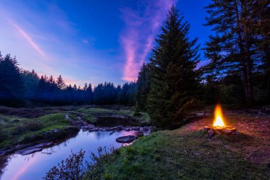 Batı Virginia 'daki Dolly Sods vahşi doğasında, Red Creek' in sol çatalının yanında bir kamp ateşi yanıyor. Blackbird Knob Trail 'in geçtiği yerde. Pembe bulutlar gün batımında suya yansıyor..
