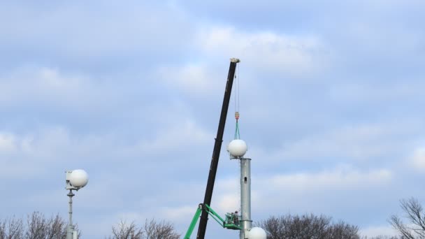 一个5G塔由建筑工人安装在一个空中工作平台上 用起重机把一个圆形的白色物体放回原处 — 图库视频影像