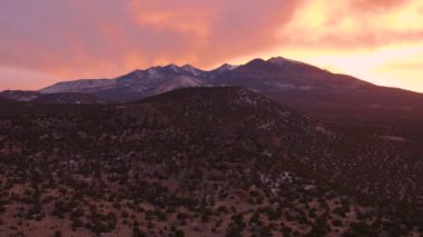 Arizona Flagstaff 'ın kuzeyindeki Coconino Ulusal Ormanı ve San Francisco Tepeleri' nin günbatımında çok güzel bir hava görüntüsü. Gökyüzü pembe ve turuncu. Kamera hareket ettiriyor, kaideyi kaldırıyor..