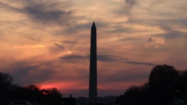 Washington, DC 'deki Washington Anıtı' nın arkasındaki bulutlar ve kıpkırmızı bir gün batımının hızlandırılması. Gökyüzünde uçak trafiği ve buhar izleri görülüyor.