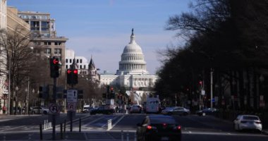 Washington, D.C. 'deki Amerikan Kongre Binası' nın yavaş çekim görüntüleri Pennsylvania Bulvarı 'ndan bir kış öğleden sonra görüldü. Araç trafiği ve yayalar ön planda hareket ediyor.
