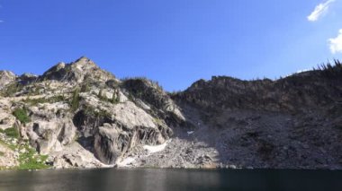 Sawtooth Ulusal Ormanı 'ndaki Lower Trail Creek Gölü' nde bir yaz akşamı engebeli bir dağ havzasının üzerinde sürüklenen bulutlar ve sudaki yansımaları. Hiç kimse görünmüyor..