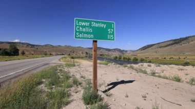 Stanley 'in girişindeki 75. Otoyol' daki yol tabelası Challis ve Salmon gibi kasabalara olan uzaklığı gösteriyor. Somon nehri akar, sığırlar otlar ve karavanı olan bir kamyon geçer..
