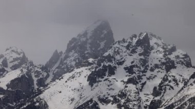 Grand Teton 'un Wyoming' deki karlı zirvesi, komşu dağlarla çevrili, bir bahar günü geç saatlerde bulutların zirvesini kısmen karartmasıyla yakalandı.