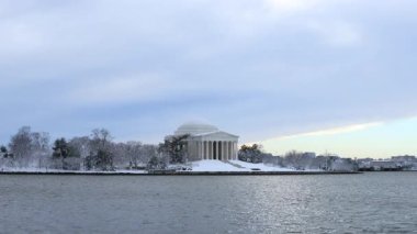 Washington, D.C. 'deki Jefferson Memorial ve Tidal Basin' de karlı bir kış gününde görüldüğü gibi. Anma töreninin önünde iki uzak insan yürüyor. Gökyüzü bulutlu. Kazlar gökyüzünde uçar.
