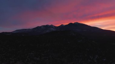 Flagstaff, Arizona 'nın kuzeyindeki Humphreys Tepesi ve Kachina Tepeleri' nin arkasında mor ve kırmızı bir günbatımı gökyüzü. Havadan çekilen bir kamera..