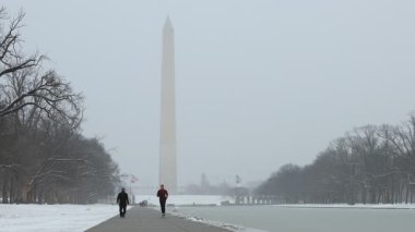 Washington, DC - ABD - Şubat 12021: Karlı bir günde Lincoln Memorial Yansıma Havuzu yakınlarında bir koşucu ve maskeli bir yaya. Arka planda Washington Anıtı görülüyor.