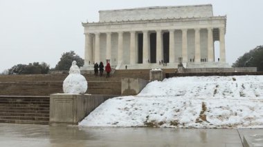 Turistler karlı bir kış gününde Washington, D.C. 'deki Lincoln Anıtı' nı ziyaret ederler. Bir kardan adam ve yandan esen kar ve dondurucu yağmur ön planda görülüyor..