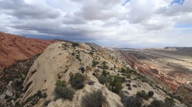 Bir grup yürüyüşçü, Utah 'taki Capitol Reef Ulusal Parkı' nda bulunan 160 km 'lik jeolojik bir özellik olan Waterpocket Katliamı' nın batı yamacından geçiyor. Gökyüzünde kara yağmur bulutları görülür..