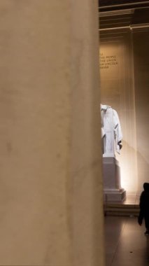 Lincoln Anıtı 'nı ziyaret eden turistlerin zaman aşımı. Kamera, Abraham Lincoln 'ün heykelini ortaya çıkarmak için mermer bir sütunun arkasından sağa doğru izler. Dikey bileşim.