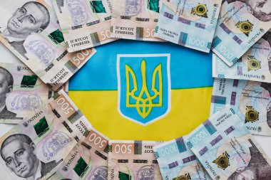 Ukrayna bayrağının arka planında Ukrayna para birimi Hryvnia. Ukrayna 'daki savaşla ilgili olarak vatandaşlara devlet yardımı.