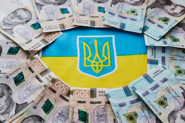 Ukrayna bayrağının arka planında Ukrayna para birimi Hryvnia. Ukrayna 'daki savaşla ilgili olarak vatandaşlara devlet yardımı.