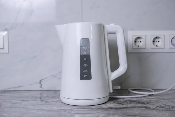 A woman draws water into an electric kettle in the background of the kitchen. It's time for breakfast and tea. Modern electric kettle. Kettle for boiling water.