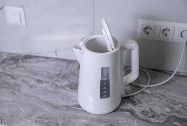 A woman draws water into an electric kettle in the background of the kitchen. It's time for breakfast and tea. Modern electric kettle. Kettle for boiling water.