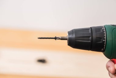 Beyaz arka planda bir adamın elinde elektrikli tornavida ve bir ağaç zemininde