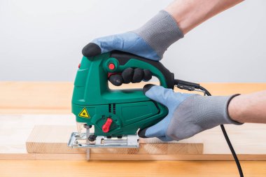 Tahta bir masada elektrikli bir yapbozla çalışan bir adam. Eldivenli ve mezurasız ve mezuralı.