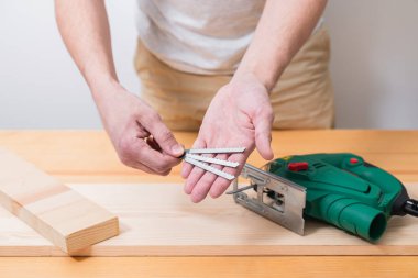 Tahta bir masada elektrikli bir yapbozla çalışan bir adam. Eldivenli ve mezurasız ve mezuralı.