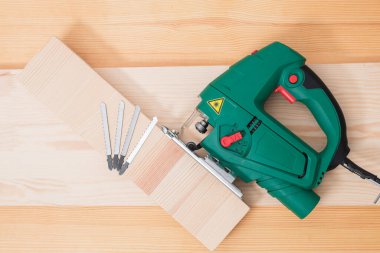 Tahta bir masada elektrikli bir yapbozla çalışan bir adam. Eldivenli ve mezurasız ve mezuralı.