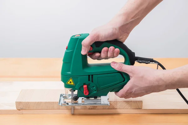 stock image A man works with an electric jigsaw for wood on a wooden table with and without gloves and measures with a tape measure