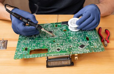 Bir adam elinde bir lehim makinesi tutar ve bir mikro devre lehimler.