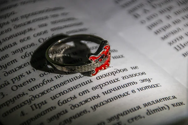A ring in the form of a red guitar lies on the page of a book close-up