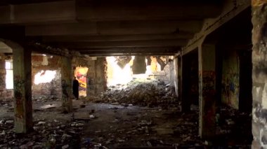 Siyah uzun paltolu genç bir adam yıkılmış bir binanın içinde yürüyor.