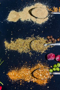 Baharatlar diğer renkli ürünlerin yanında çay kaşığı üzerine koyu mavi bir arkaplana saçılmış.