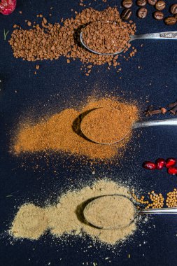 Baharatlar diğer renkli ürünlerin yanında çay kaşığı üzerine koyu mavi bir arkaplana saçılmış.