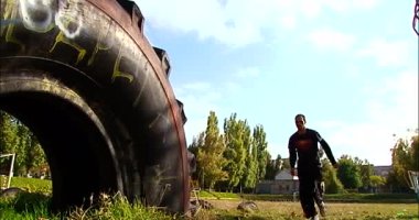 Adamın biri yavaş çekimde büyük bir traktör lastiğiyle parka akrobatik bir atlayış yapıyor.