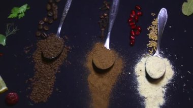 Baharatlar, videodaki siyah bir arka planda, besin maddeleri arasında beş tatlı kaşığına dağılmış durumda.