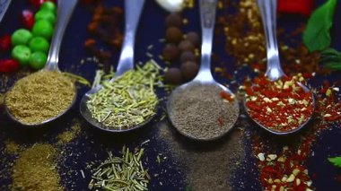 Baharatlar, videodaki karanlık bir arka planda, besin maddeleri arasında beş çay kaşığı üzerine dağılmış durumda.