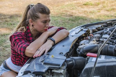 Siyah ve kırmızı kareli gömlekli güzel kız araba motorunu tamir etmeyi düşünüyor.