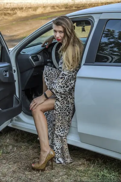 Mavi gözlü, güzel, benekli elbiseli, uzun saçlı, beyaz bir arabanın kapısından dışarı bakan güzel bir kız.