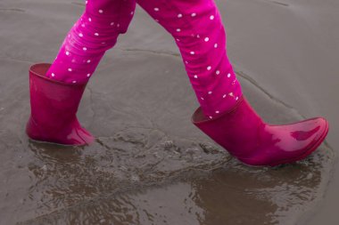 Su birikintisi olan pembe lastik çizmeli küçük kız.