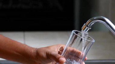 Erkek elleri mutfak musluğundan cam bir fincana taze musluk suyu döküyor. 