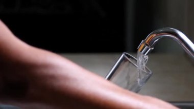 Erkek elleri mutfak musluğundan cam bir fincana taze musluk suyu döküyor. 