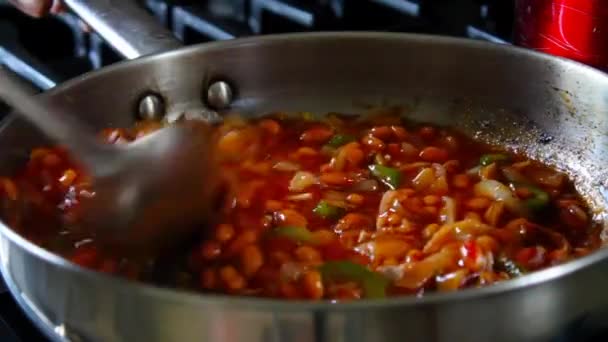 これはキッチンストーブに鍋にスプーンで美味しい焼き豆をかき混ぜる手のビデオショットです — ストック動画